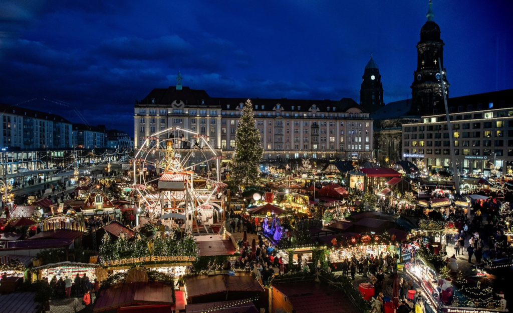 Illuminated Christmas market stalls, Ferris wheel and Christmas tree in Dresden, Germany, at dusk.