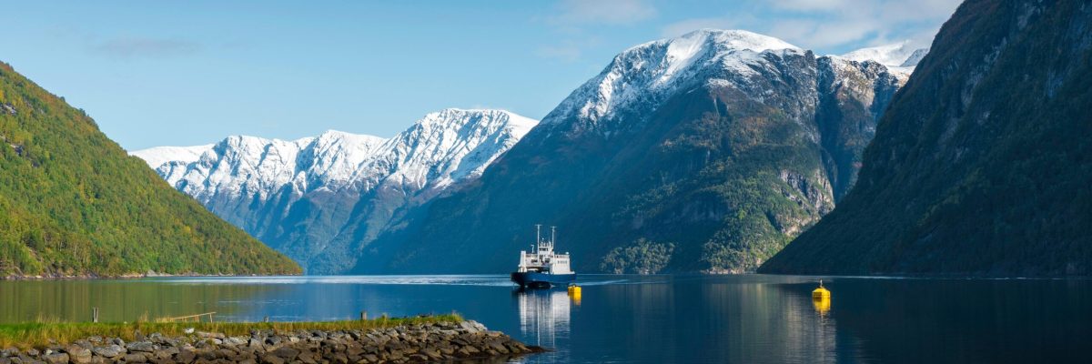 Reflective ferry traversing a stunning Norwegian fjord surrounded by snow-capped mountains.