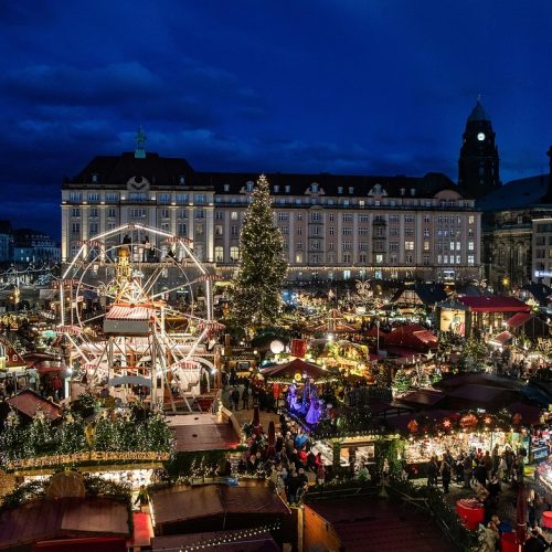 Illuminated Christmas market stalls, Ferris wheel and Christmas tree in Dresden, Germany, at dusk.